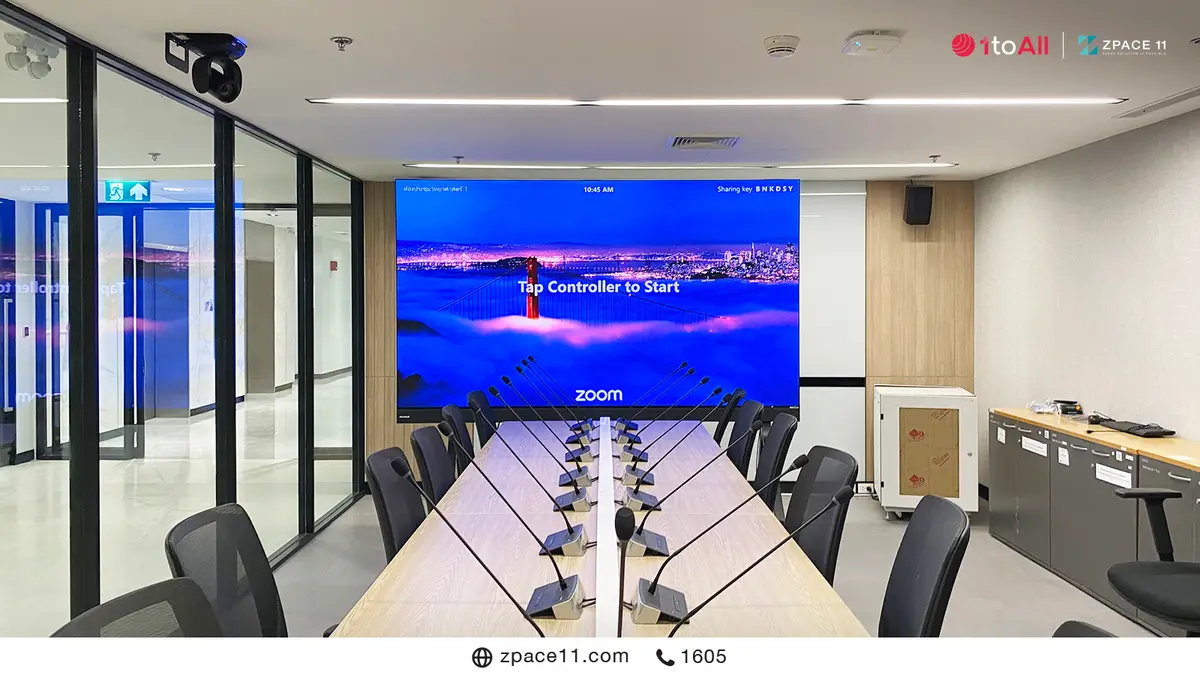 ห้องประชุมที่มีจอ LED ผนังแสดงหน้า Zoom Rooms และไมโครโฟนตั้งโต๊ะ