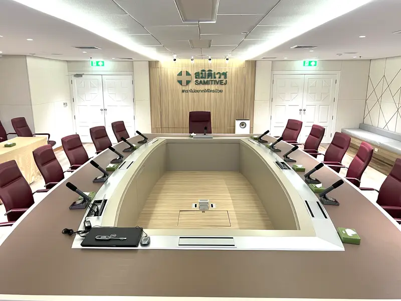 ห้องประชุมผู้บริหารที่มีโต๊ะประชุมทรงสี่เหลี่ยมเว้นกลาง ไมค์คอห่านทุกที่นั่ง และเก้าอี้สีแดงเข้ม