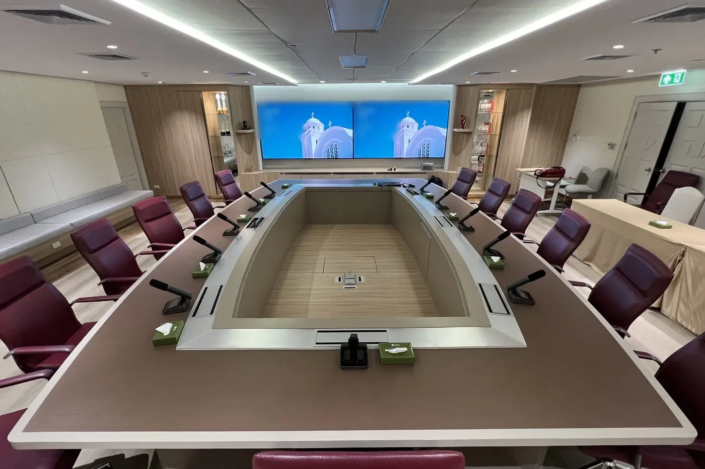 ห้องประชุมผู้บริหารพร้อมโต๊ะแบบเว้นช่องตรงกลาง ไมโครโฟนทุกที่นั่ง และจอติดผนังสองจอ