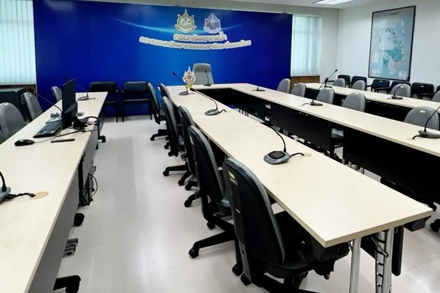 ห้องประชุมพร้อมโต๊ะและไมโครโฟนเรียงแถว หน้าผนังสีน้ำเงิน