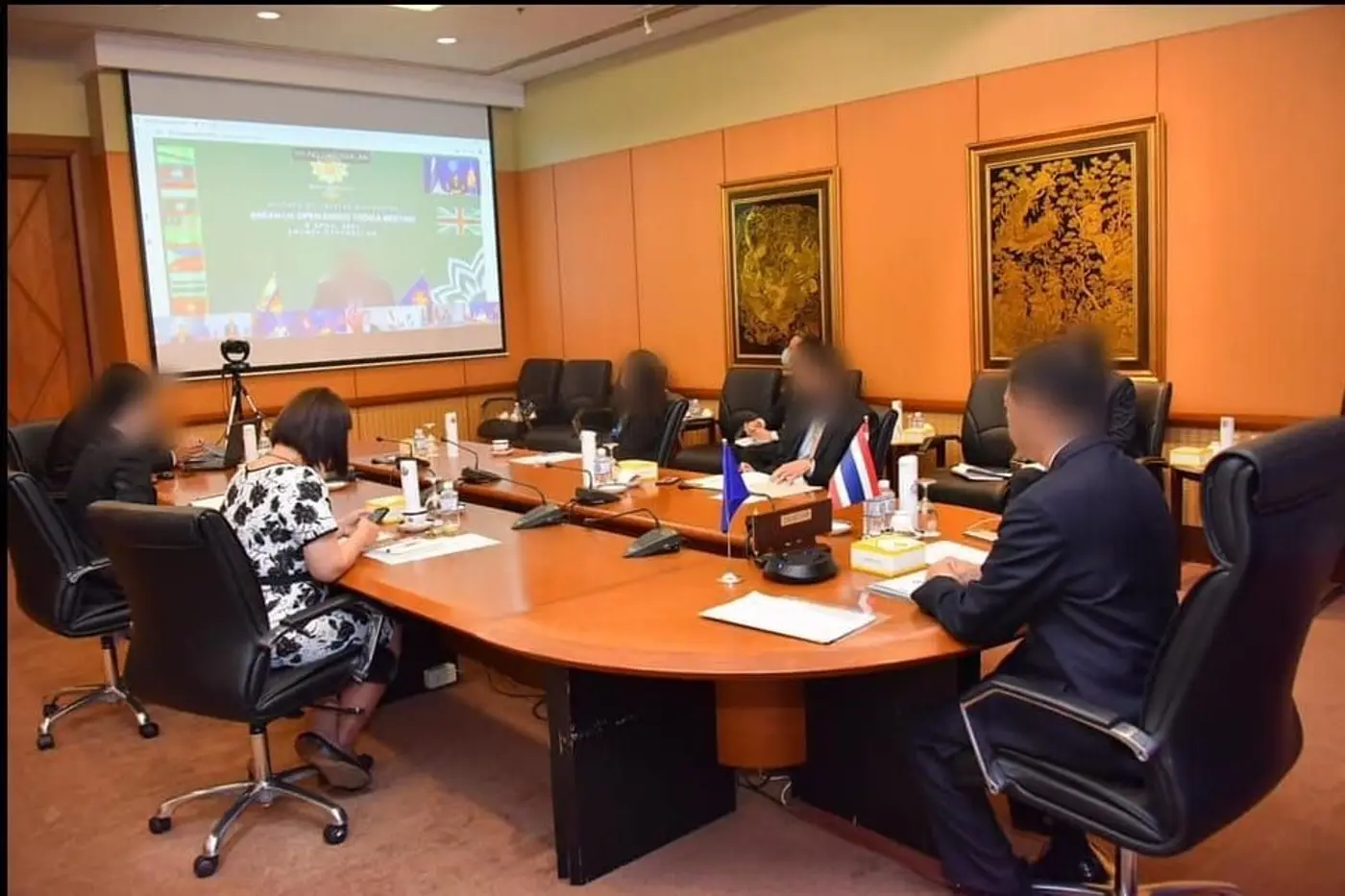การประชุมทางไกลที่โต๊ะประชุมทรงโค้ง พร้อมไมโครโฟนตั้งโต๊ะ ธง และจอโปรเจกเตอร์