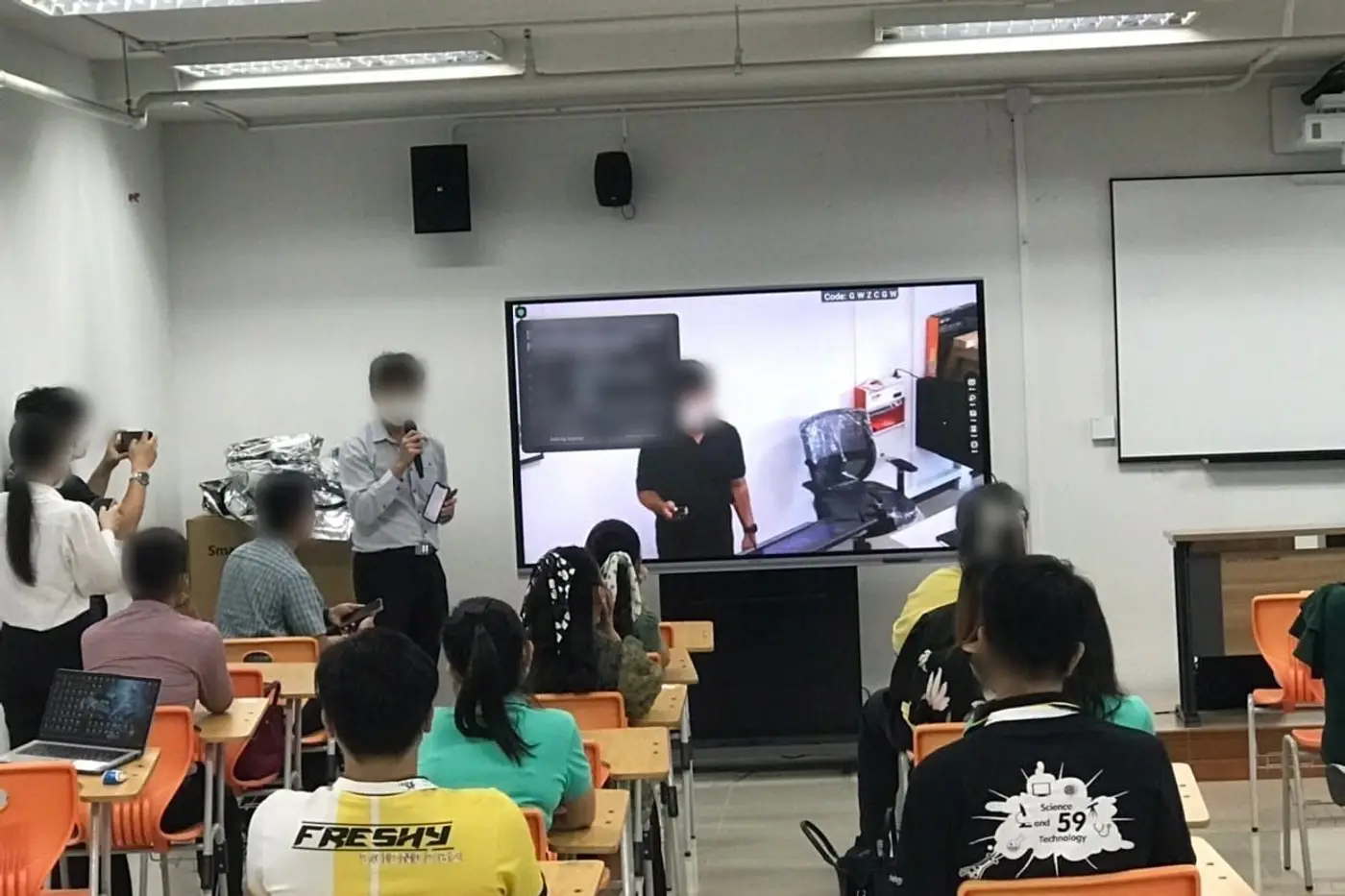 ห้องเรียนพร้อมจอขนาดใหญ่ที่กำลังประชุมทางไกล ลำโพงติดผนัง และโต๊ะเรียน