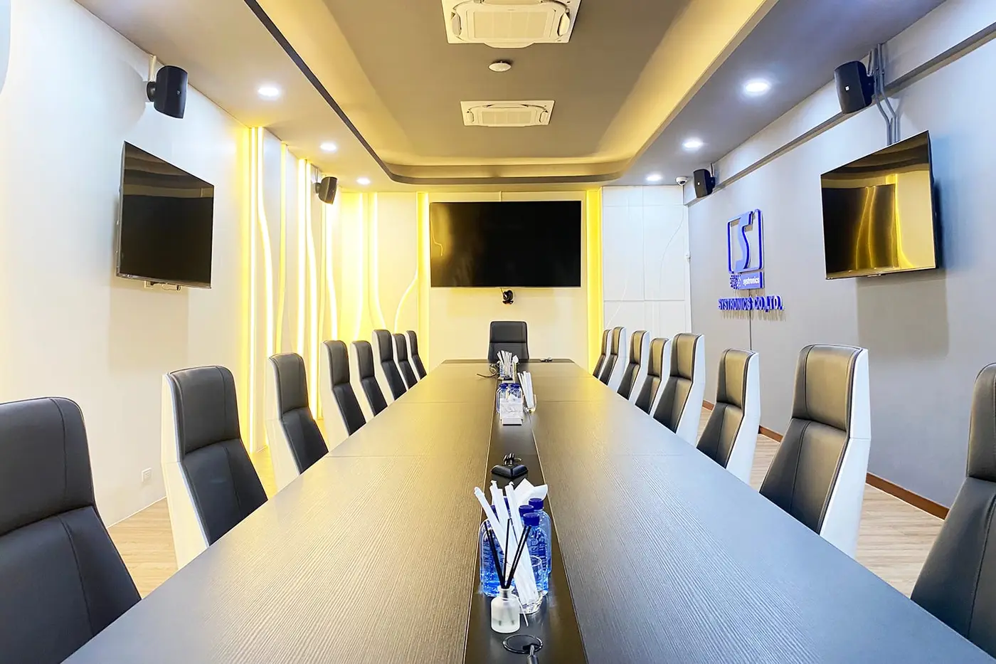ห้องประชุมผู้บริหารแบบยาว พร้อมจอติดผนังสามจอและลำโพงติดผนัง